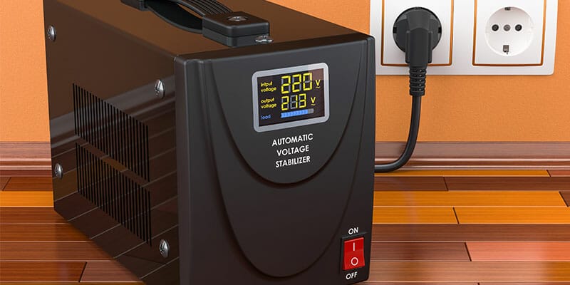 A black color voltage stabilizer kept on a wooden table is connected to a switch board.