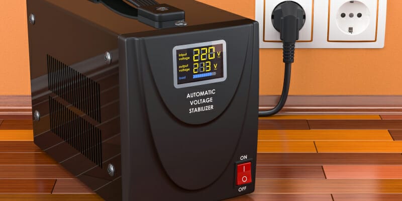 An automatic voltage stabilizer on the wooden floor is connected to an outlet.